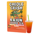 A detailed shot of one Creole Crush packet (featuring the alligator and fruit design) placed next to a clear cup containing the prepared, two-tone red and orange loaded tea.